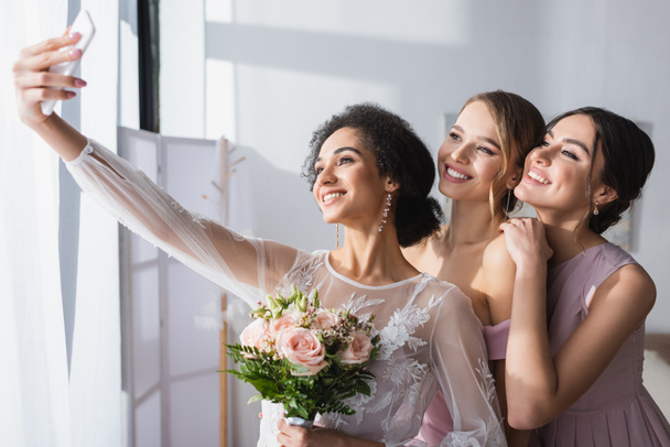 junge afrikanisch-amerikanische Braut macht Selfie mit fröhlichen Brautjungfern zu Hause - Foto, Bild
