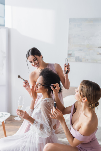 cheerful bridesmaids doing visage to african american bride holding champagne glass - Foto, imagen
