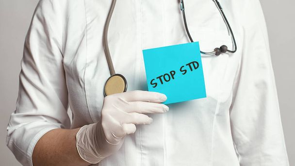Katsaus lääkäriin valkoisessa takissa ja steriileissä käsineissä, joissa on merkintä tekstillä - STOP STD. Lääketieteellinen käsite - Valokuva, kuva