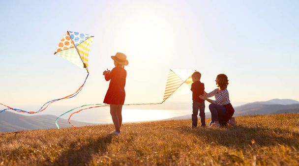 Gelukkige familie moeder en kinderen lanceren een vlieger op de natuur bij zonsondergang - Foto, afbeelding