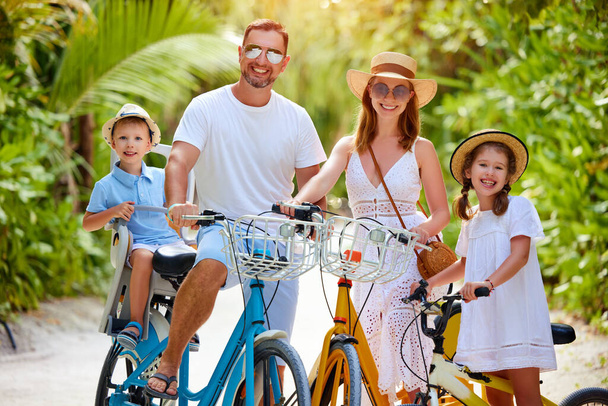 Happy family: rodiče a děti v letních šatech si užívají výlet na kole v zeleném tropickém parku během letních prázdnin - Fotografie, Obrázek