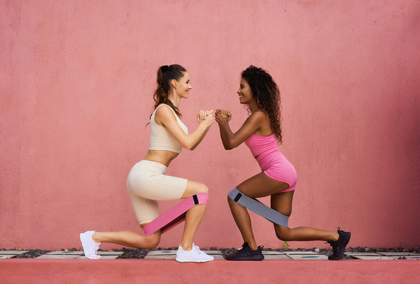 Photo fitness girls in a stylish sports suit squats with rubber bands on the background of a pink wall. Sports woman squats, sits. Copy ad space - Photo, Image