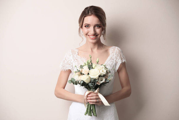 Young bride with beautiful wedding bouquet on beige background - Foto, imagen