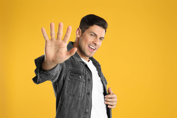 Man showing number five with his hand on yellow background - Fotó, kép