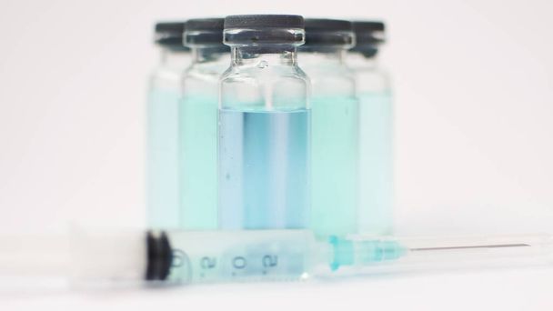 Vaccin flacon, ampoules en verre avec liquide transparent et bleu, une seringue est couchée près sur fond blanc, concept mondial de vaccination - Photo, image