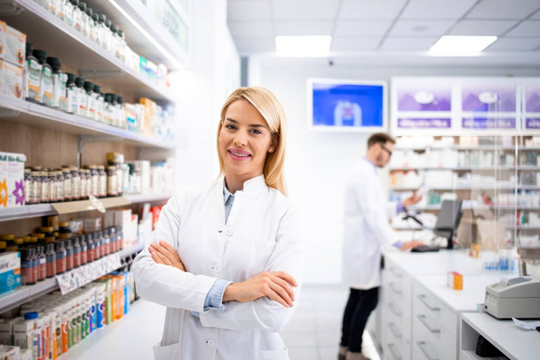 Portret pięknej blond farmaceutki stojącej w aptece przy półce z lekami. - Zdjęcie, obraz