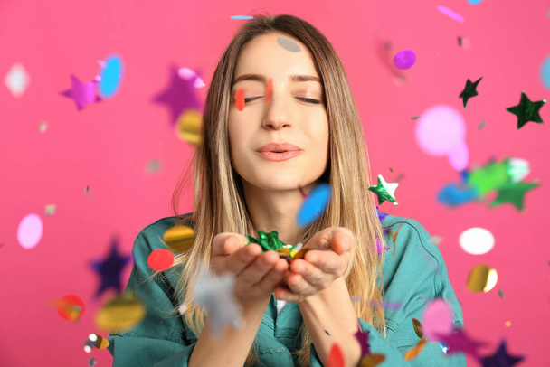 Happy woman blowing confetti on pink background - Foto, Imagem