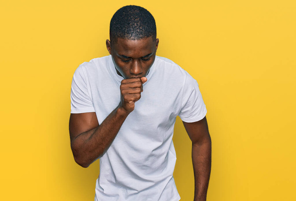 風邪や気管支炎の症状として、カジュアルな白いTシャツを着て咳をしている若いアフリカ系アメリカ人男性。ヘルスケアの概念.  - 写真・画像
