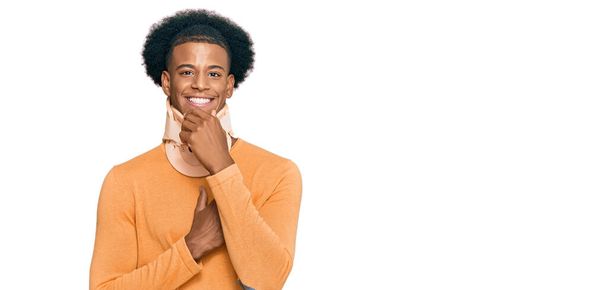 Uomo afro-americano con capelli afro con collo cervicale guardando fiducioso la fotocamera con sorriso a braccia incrociate e mano alzata sul mento. pensare positivo.  - Foto, immagini