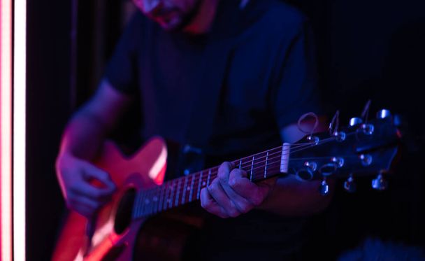 Un uomo suona una chitarra acustica in una stanza buia. Live performance, concerto acustico. - Foto, immagini