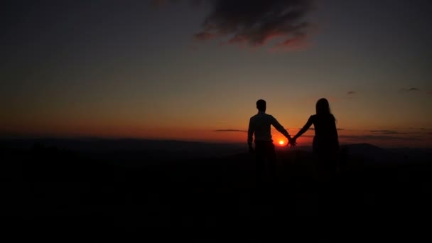 Romantisch outdoor portret van de paar silhouetten die elkaar handen geven, knuffelen en kussen tijdens de zonsondergang. Prachtig landschap. De vrouw houdt het boeket vast.. - Video