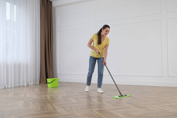 Young woman cleaning floor with mop in empty room - Photo, image