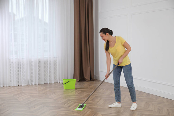 Young woman cleaning floor with mop in empty room - Foto, Imagen