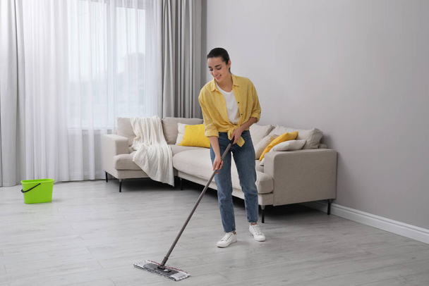 Young woman cleaning floor with mop in living room - Photo, image