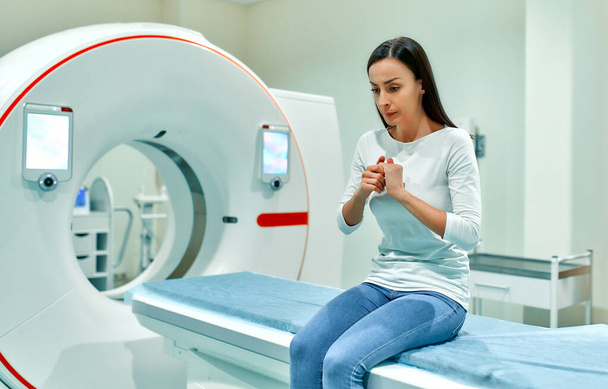 Na lůžku CT nebo MRI přístroje sedí rozrušený, smutný a vyděšený pacient. V lékařské laboratoři se špičkovým vybavením. - Fotografie, Obrázek