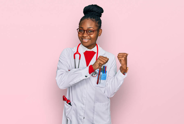 医者の制服を着た若いアフリカ系アメリカ人女性手と親指で後ろを指差す聴診器自信を持って笑って  - 写真・画像