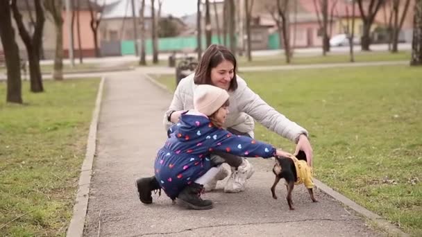 Bella giovane mamma a piedi con figlia e cagnolino. Felice famiglia a piedi all'aperto con animale domestico durante la quarantena - Filmati, video