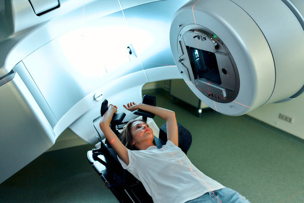Μια νεαρή γυναίκα υποβάλλεται σε ακτινοθεραπεία για καρκίνο σε ένα σύγχρονο νοσοκομείο καρκίνου. Θεραπεία καρκίνου, σύγχρονο ιατρικό γραμμικό επιταχυντή. - Φωτογραφία, εικόνα