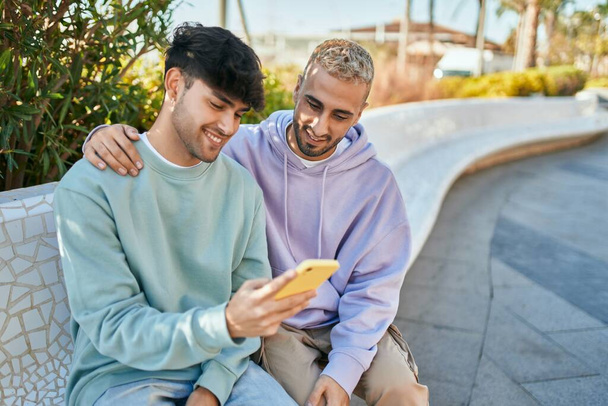Молодая пара геев улыбается счастливо, используя смартфон в городе. - Фото, изображение