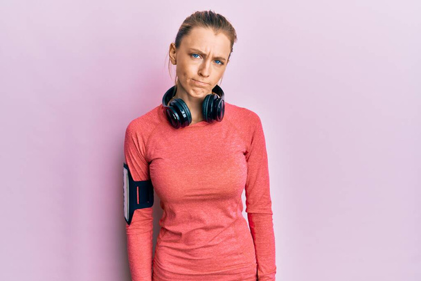 Beautiful caucasian woman wearing sportswear and arm band skeptic and nervous, frowning upset because of problem. negative person.  - Photo, Image