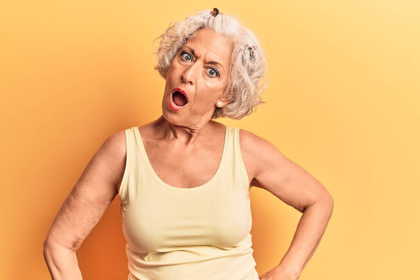 Ηλικιωμένη γκριζομάλλα γυναίκα που φοράει καθημερινά ρούχα σε κατάσταση σοκ, δείχνοντας σκεπτική και σαρκαστική, έκπληκτη με το ανοιχτό στόμα  - Φωτογραφία, εικόνα
