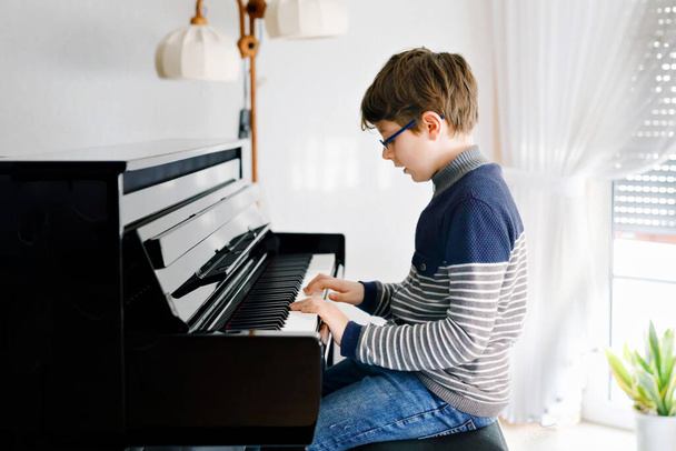A szemüveges iskolás fiú zongorázik a nappaliban. A gyerek szórakozik a hangszeren való tanulással. Tehetséges gyerek az otthoni koszorúér-vírus zárlat alatt. - Fotó, kép