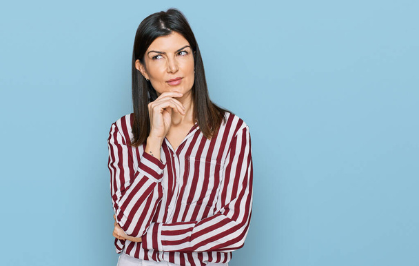 Beautiful brunette woman wearing striped shirt with hand on chin thinking about question, pensive expression. smiling with thoughtful face. doubt concept.  - Photo, Image