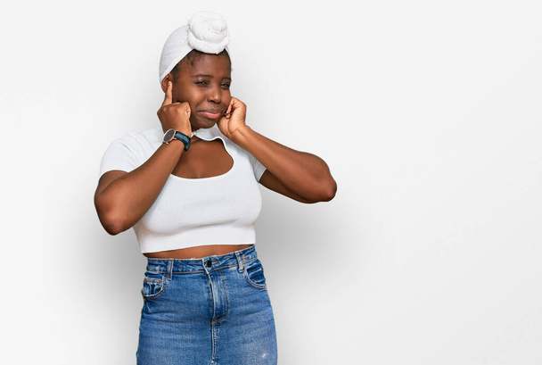 Junge Afrikanerin mit Turban trägt Turban über isoliertem Hintergrund und verdeckt Ohren mit Fingern mit genervtem Gesichtsausdruck wegen des Geräusches lauter Musik. Gehörloses Konzept.  - Foto, Bild