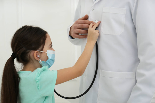 Little girl playing with pediatrician during visit in hospital. Patient wearing protective mask - Φωτογραφία, εικόνα
