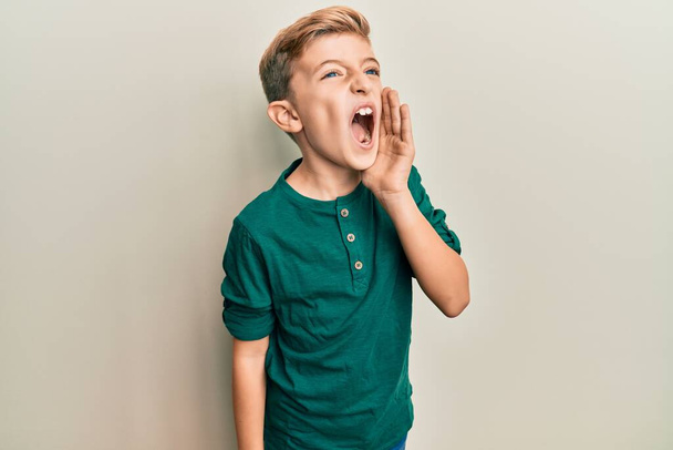 Little caucasian boy kid wearing casual clothes shouting and screaming loud to side with hand on mouth. communication concept.  - Фото, зображення