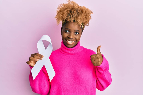 若いですアフリカ人女性とともにアフロ髪保持ピンク癌リボン笑顔と正、親指アップ行う優れた承認サイン  - 写真・画像