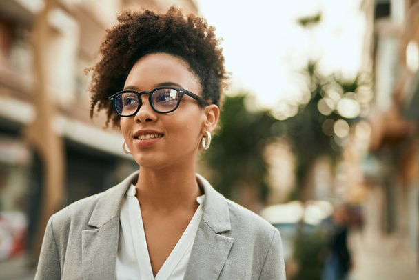 Νεαρή αφροαμερικανή επιχειρηματίας χαμογελά ευτυχισμένη στέκεται στην πόλη. - Φωτογραφία, εικόνα
