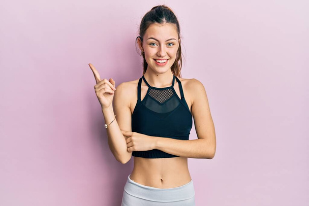Young brunette woman wearing sportswear smiling happy pointing with hand and finger to the side  - Foto, Bild