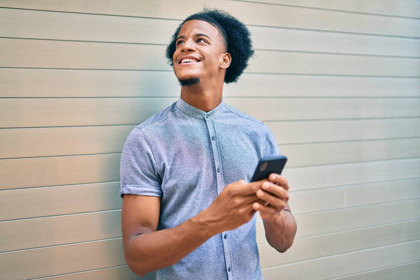 Giovane uomo afroamericano sorridente felice utilizzando smartphone in città. - Foto, immagini