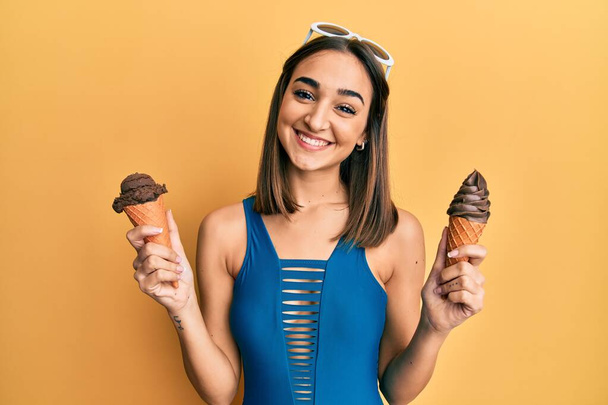 Young brunette girl wearing swimwear holding two ice cream cones smiling with a happy and cool smile on face. showing teeth.  - Φωτογραφία, εικόνα