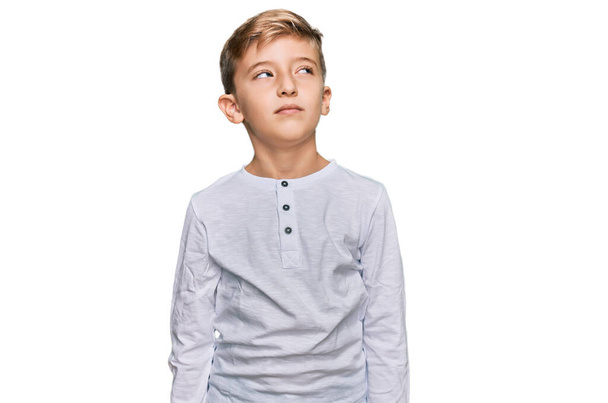 Kis kaukázusi fiú gyerek alkalmi ruhát visel mosolyog oldalra néz, és félrenéz gondolkodás közben.  - Fotó, kép