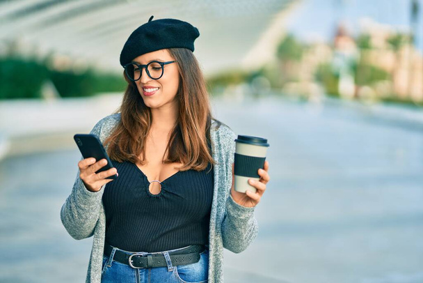 Jonge latijnse vrouw met smartphone die koffie drinkt in de stad. - Foto, afbeelding