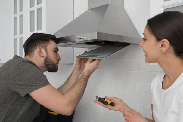 Man repairing modern cooker hood and woman in kitchen - Photo, Image
