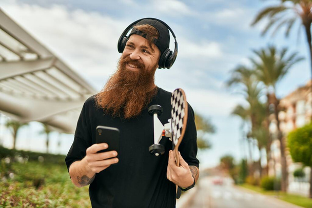 Mladý irský bruslař muž pomocí smartphone a sluchátka ve městě. - Fotografie, Obrázek