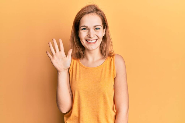Молодая белая женщина в непринужденном стиле в рубашке без рукавов показывает и показывает пальцами номер пять улыбаясь уверенно и счастливо.  - Фото, изображение