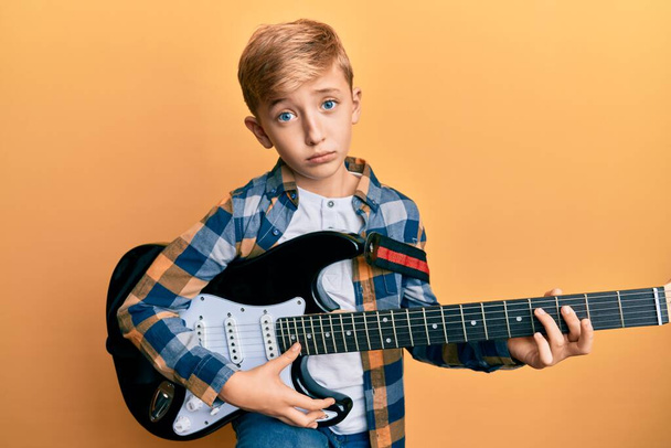 Petit garçon caucasien jouant de la guitare électrique déprimé et inquiet pour la détresse, pleurant en colère et effrayé. triste expression.  - Photo, image