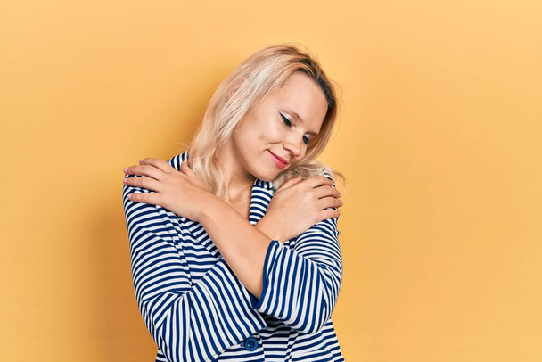Beautiful caucasian blonde woman wearing business jacket hugging oneself happy and positive, smiling confident. self love and self care  - Foto, Imagem