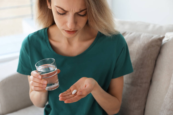 Upset young woman with abortion pill and glass of water at home, closeup - Fotografie, Obrázek