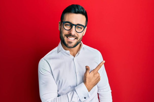 Young hispanic businessman wearing shirt and glasses cheerful with a smile of face pointing with hand and finger up to the side with happy and natural expression on face  - Fotoğraf, Görsel