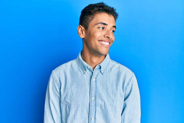 Junger gutaussehender afrikanisch-amerikanischer Mann trägt lässige Kleidung, die zur Seite schaut, entspannte Profilpose mit natürlichem Gesicht und selbstbewusstem Lächeln.  - Foto, Bild