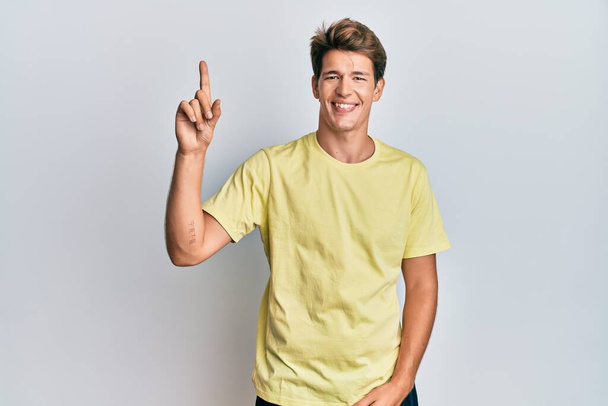 Handsome caucasian man wearing casual clothes showing and pointing up with finger number one while smiling confident and happy.  - Photo, Image