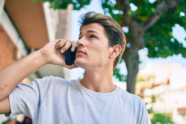 Ciddi bir suratı olan beyaz bir genç şehirde akıllı telefondan konuşuyor.. - Fotoğraf, Görsel