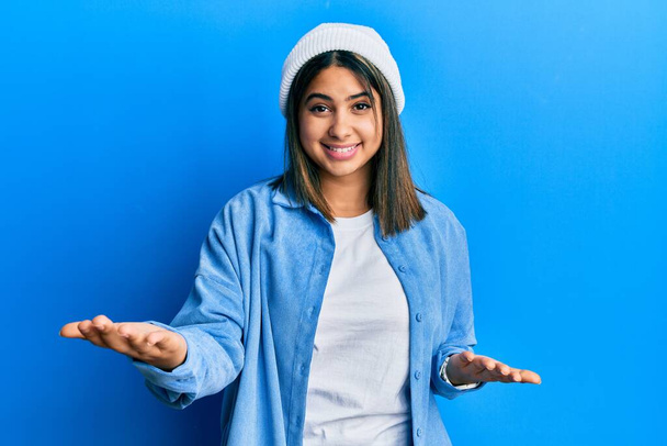 Nuori latino nainen yllään söpö villa korkki hymyilevä iloinen avosylin kuin ystävällinen tervetullut, positiivinen ja luottavainen tervehdys  - Valokuva, kuva