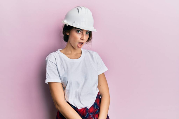 Young caucasian woman wearing hardhat afraid and shocked with surprise expression, fear and excited face.  - Photo, Image