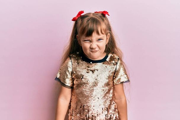 Маленькая кавказская девочка в праздничных блестках одевается скептически и нервно, хмурясь из-за проблем. отрицательный человек.  - Фото, изображение